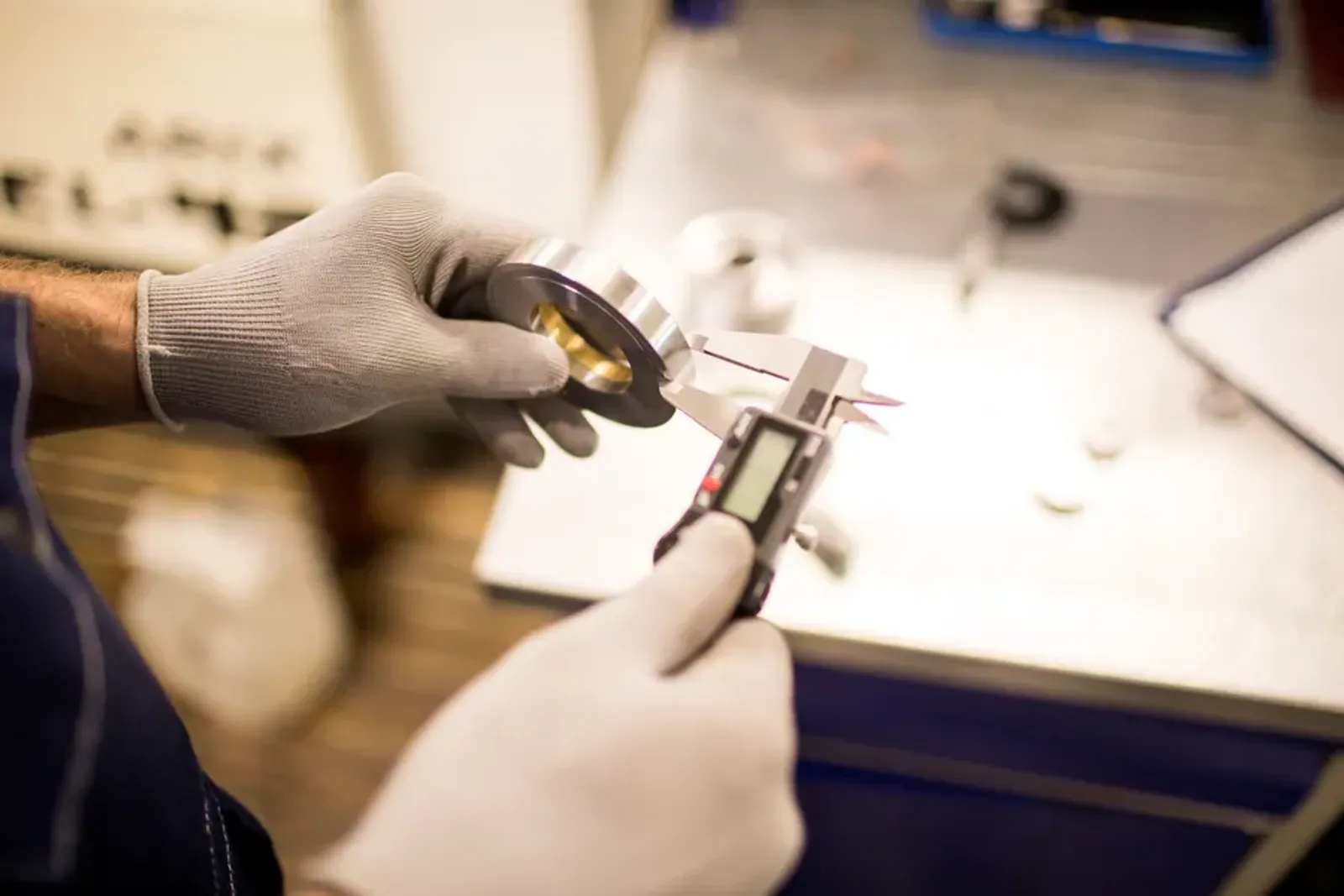 Hands measuring a machined part with digital calipers