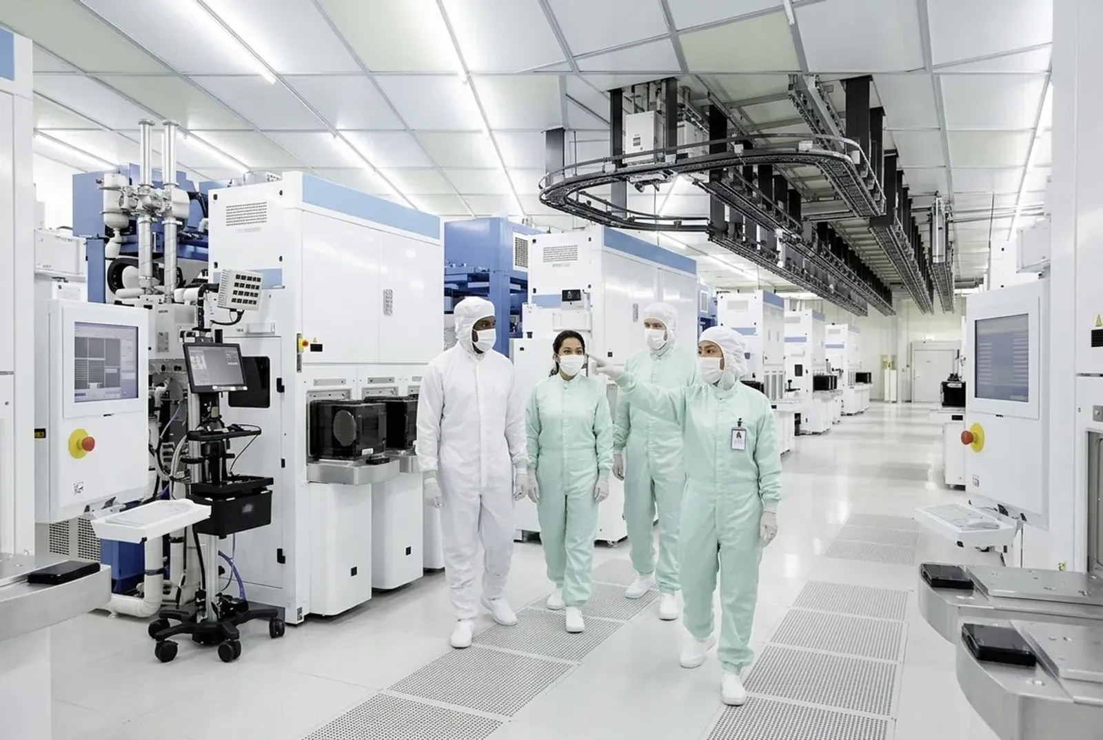 Visitors in cleanroom suits being guided through a semiconductor fab aisle