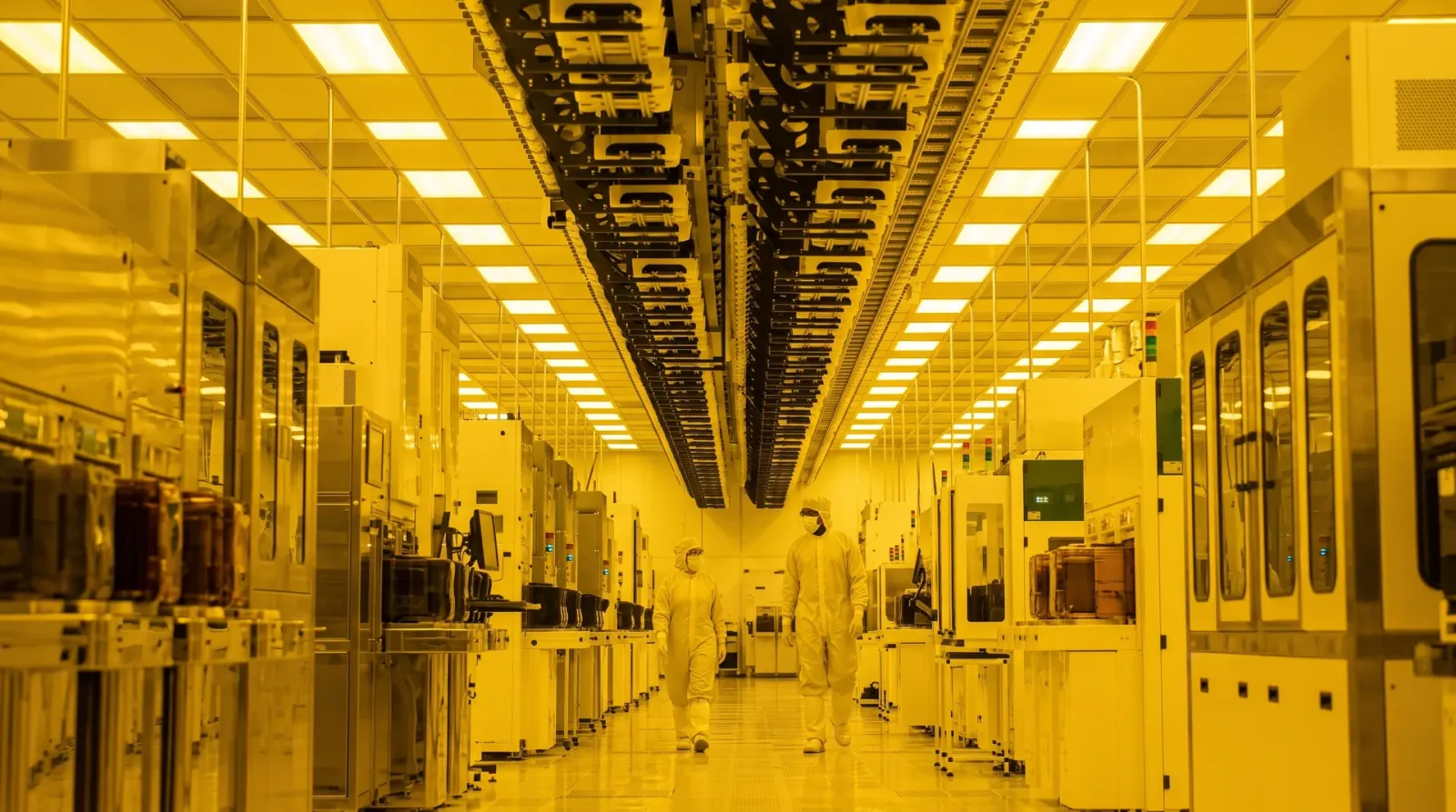 Technicians in the distance down a long yellow-lit cleanroom aisle