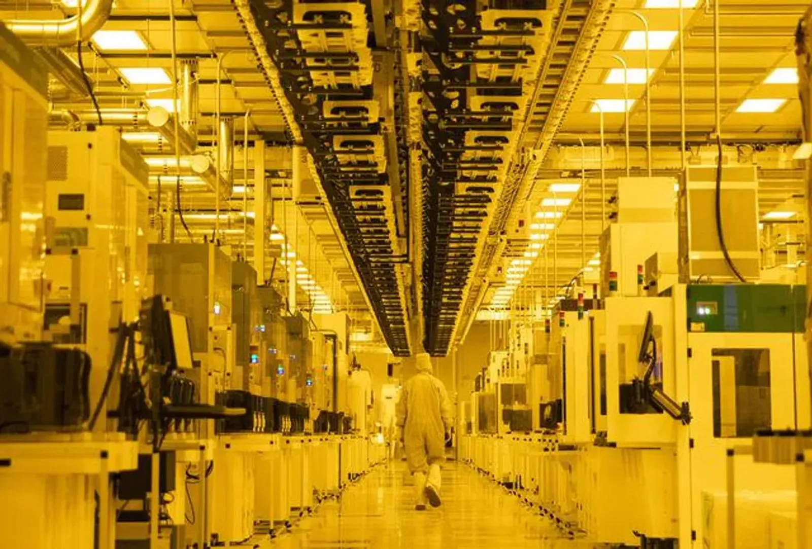 Technician in cleanroom garb walking between rows of semiconductor equipment